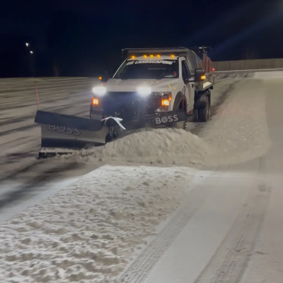 Plow truck clearing and salting a parking lot at night